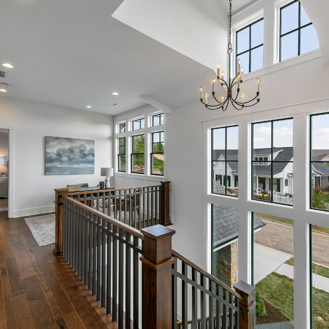 Upper landing with wood railing, chandelier and tall windows in Southern Belle, a custom home by Mike Stevens Homes