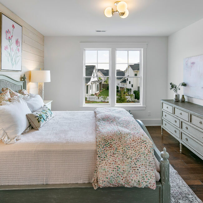 Bedroom with floral quilt, wood dresser and windows in Southern Belle, a custom home by Mike Stevens Homes