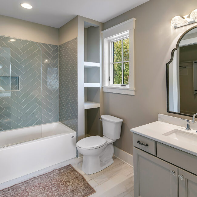 Bathroom with herringbone tile tub surround and gray vanity in Southern Belle, a custom home by Mike Stevens Homes