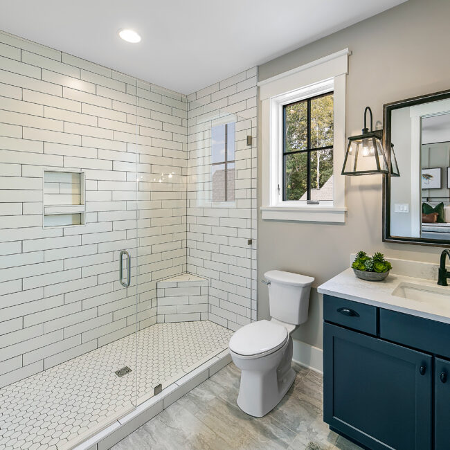 Shower with white subway tile, glass door and blue vanity in Southern Belle, a custom home by Mike Stevens Homes