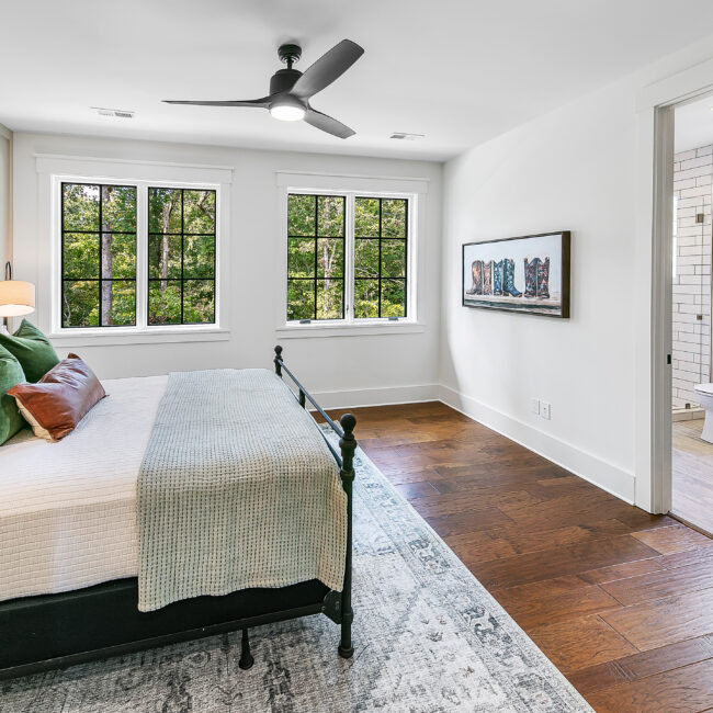 Bedroom with dark iron bed, ceiling fan and wood floors in Southern Belle, a custom home by Mike Stevens Homes