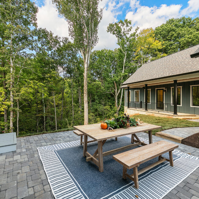 Backyard patio with wood table, bench and blue striped outdoor rug in Southern Belle, a custom home by Mike Stevens Homes