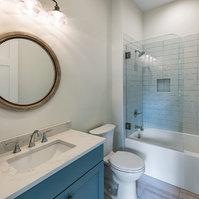 Bathroom with teal vanity, round mirror and tub-shower combination in Southern Belle, a custom home by Mike Stevens Homes