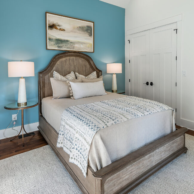Bedroom with teal accent wall, wood bed frame and table lamps in Southern Belle, a custom home by Mike Stevens Homes