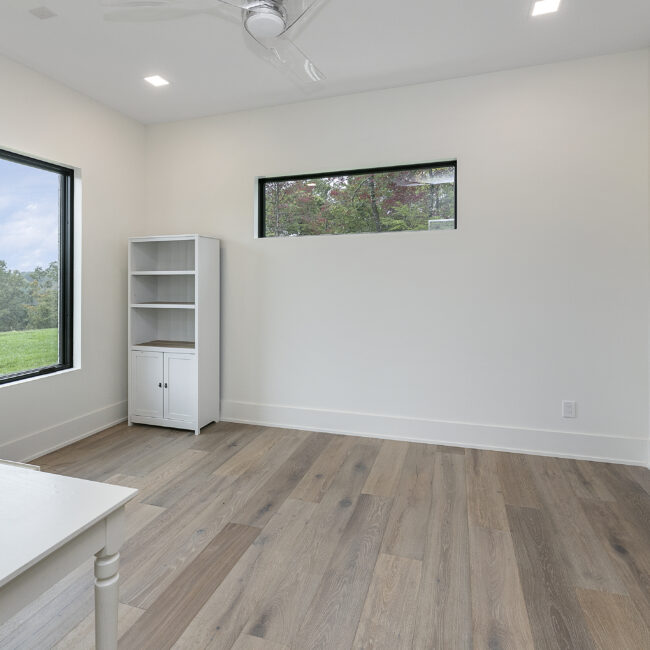 Empty room with horizontal window and wide-plank oak floors in Rocky Top Hideaway, a custom home by Mike Stevens Homes