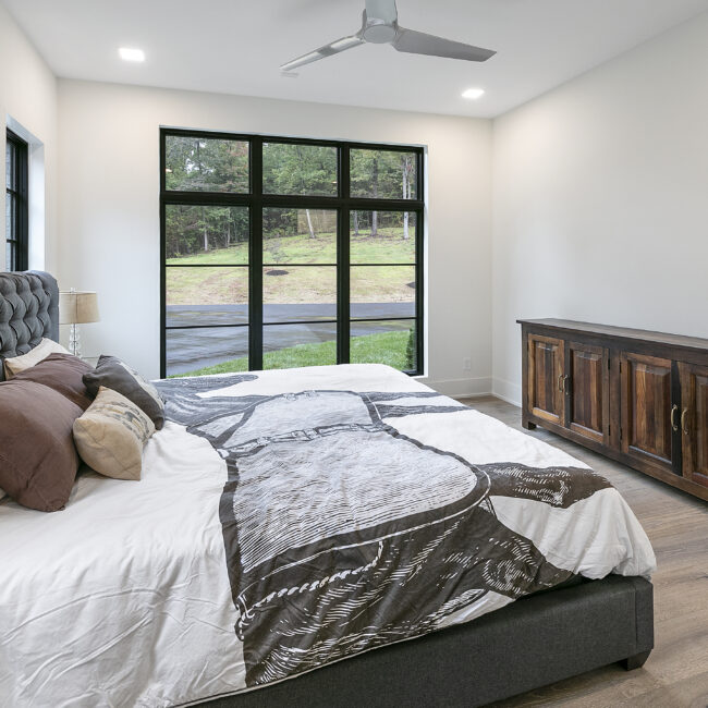 Primary bedroom with black-framed windows and gray bed in Rocky Top Hideaway, a custom home by Mike Stevens Homes