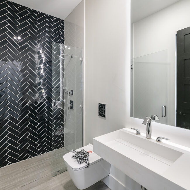 Black herringbone tile shower beside white floating vanity in Rocky Top Hideaway, a custom home by Mike Stevens Homes
