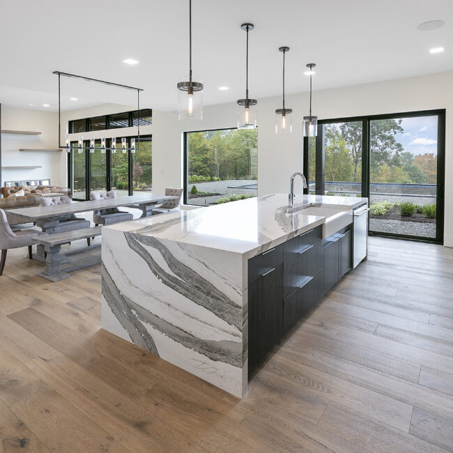 Open kitchen with waterfall quartz island and pendant lights in Rocky Top Hideaway, a custom home by Mike Stevens Homes