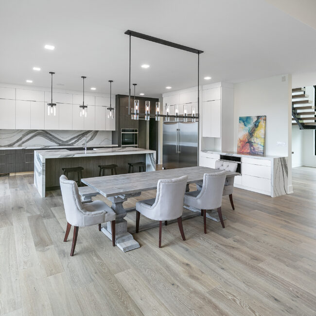 Dining table with upholstered chairs beside marble-look island in Rocky Top Hideaway, a custom home by Mike Stevens Homes