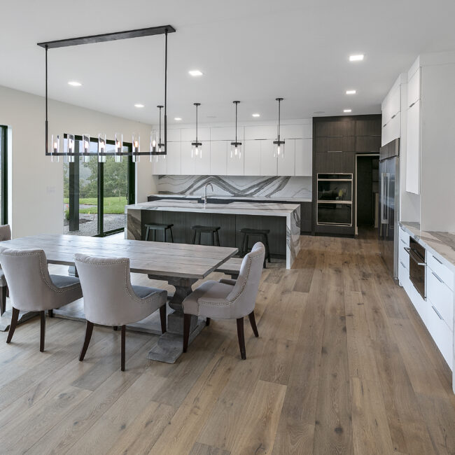 Dining area with farmhouse table beside white kitchen in Rocky Top Hideaway, a custom home by Mike Stevens Homes