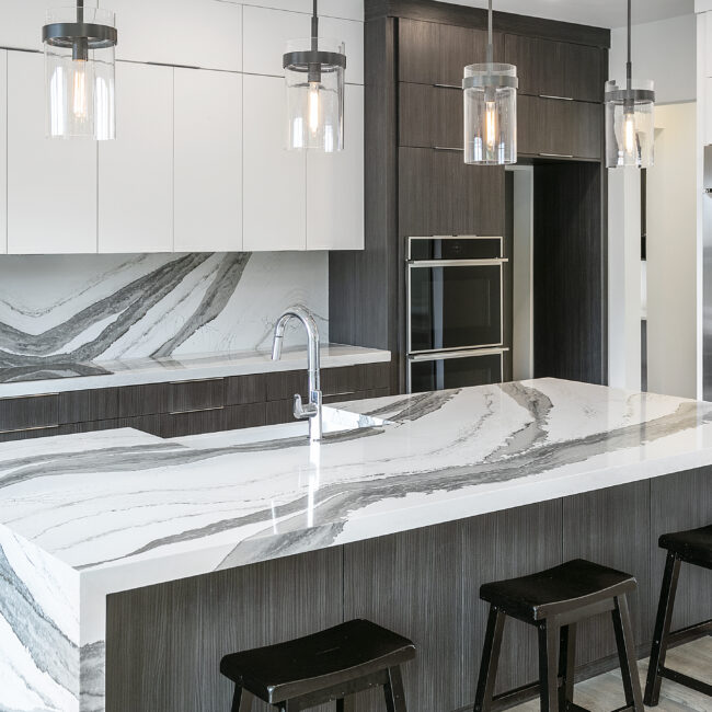 Quartz waterfall island with dark cabinets and black barstools in Rocky Top Hideaway, a custom home by Mike Stevens Homes