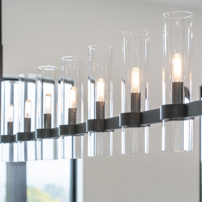 Linear glass-cylinder chandelier with Edison bulbs in Rocky Top Hideaway, a custom home by Mike Stevens Homes