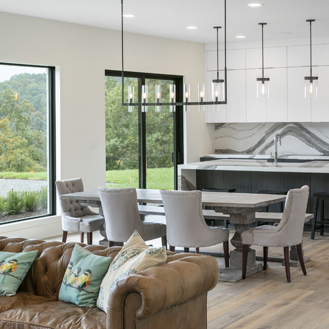 Dining area with pale chairs beside wall of glass in Rocky Top Hideaway, a custom home by Mike Stevens Homes