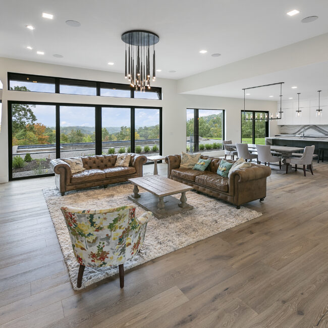 Great room with tufted leather sofas and tall windows in Rocky Top Hideaway, a custom home by Mike Stevens Homes