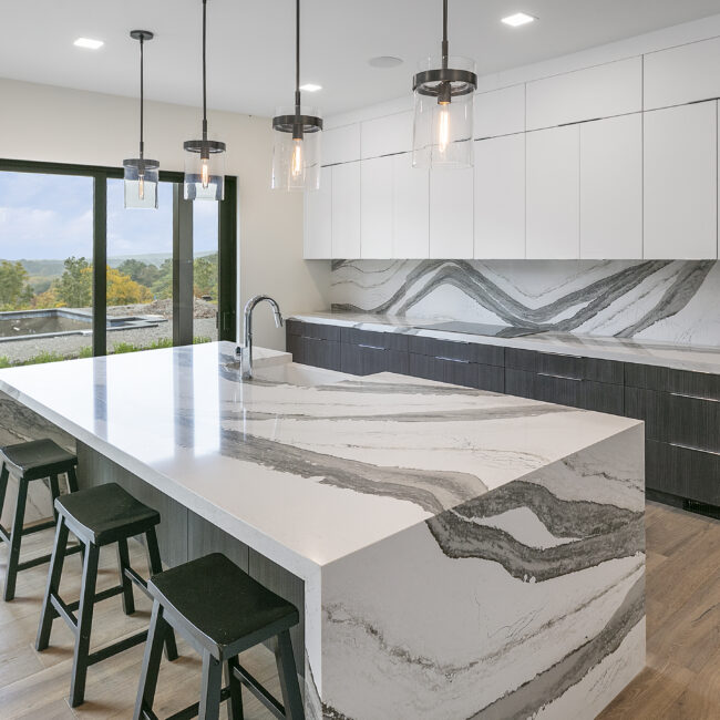 Quartz island with waterfall edge and window view of trees in Rocky Top Hideaway, a custom home by Mike Stevens Homes