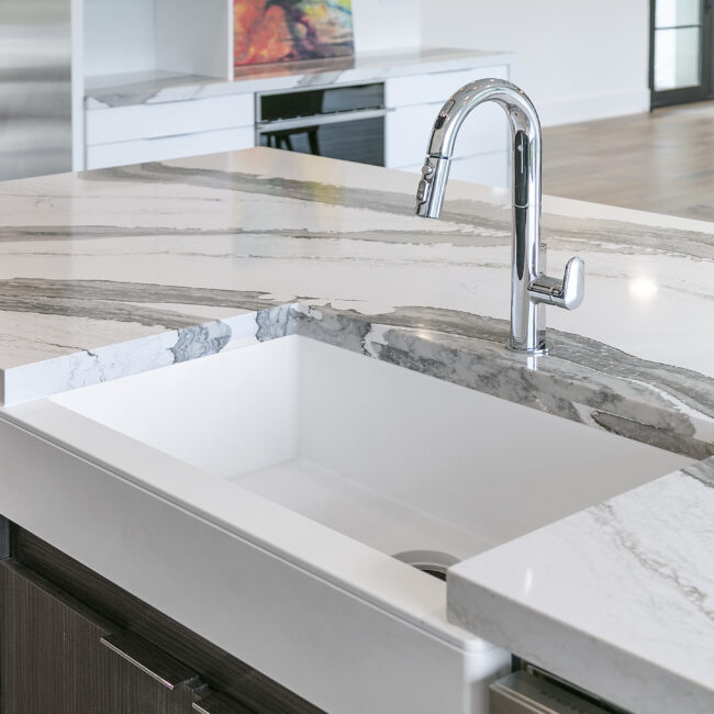 Chrome pull-down faucet over white farmhouse sink in Rocky Top Hideaway, a custom home by Mike Stevens Homes