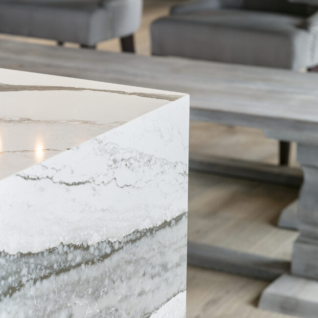 Close-up of quartz island edge beside wood dining table in Rocky Top Hideaway, a custom home by Mike Stevens Homes