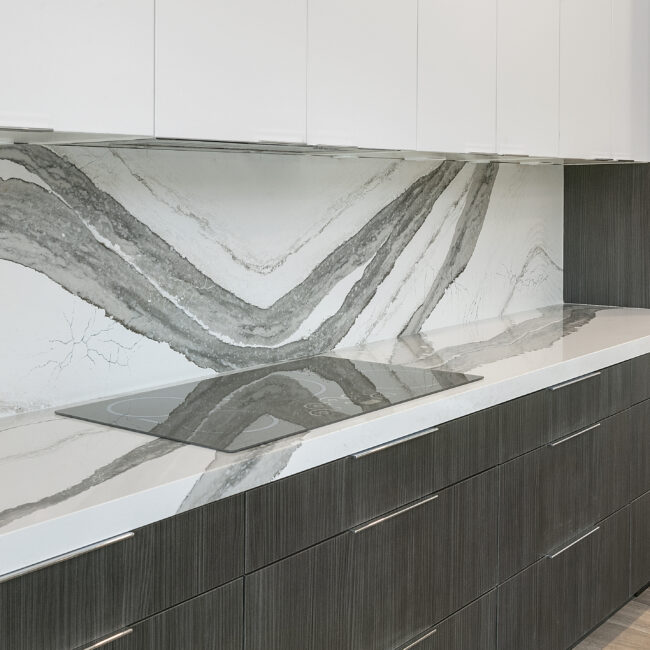 Gray-veined quartz backsplash above dark lower cabinets in Rocky Top Hideaway, a custom home by Mike Stevens Homes