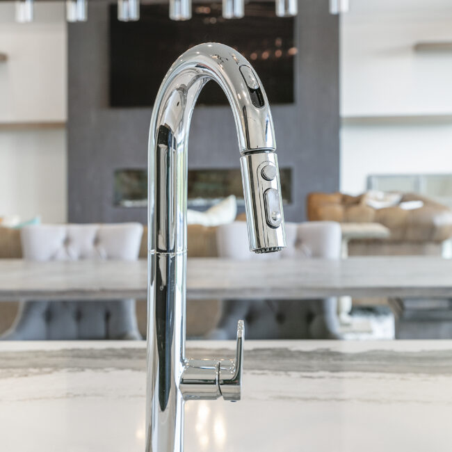 Chrome pull-down faucet with living room in soft focus in Rocky Top Hideaway, a custom home by Mike Stevens Homes