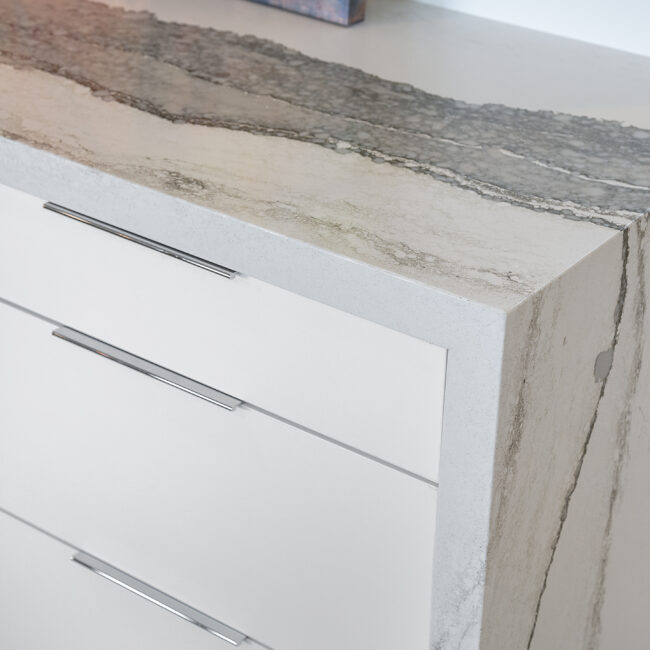 Close-up of waterfall quartz edge and white drawers in Rocky Top Hideaway, a custom home by Mike Stevens Homes