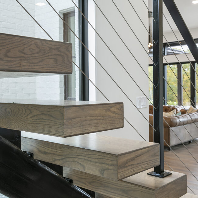 Floating wood stair treads with cable railing in Rocky Top Hideaway, a custom home by Mike Stevens Homes