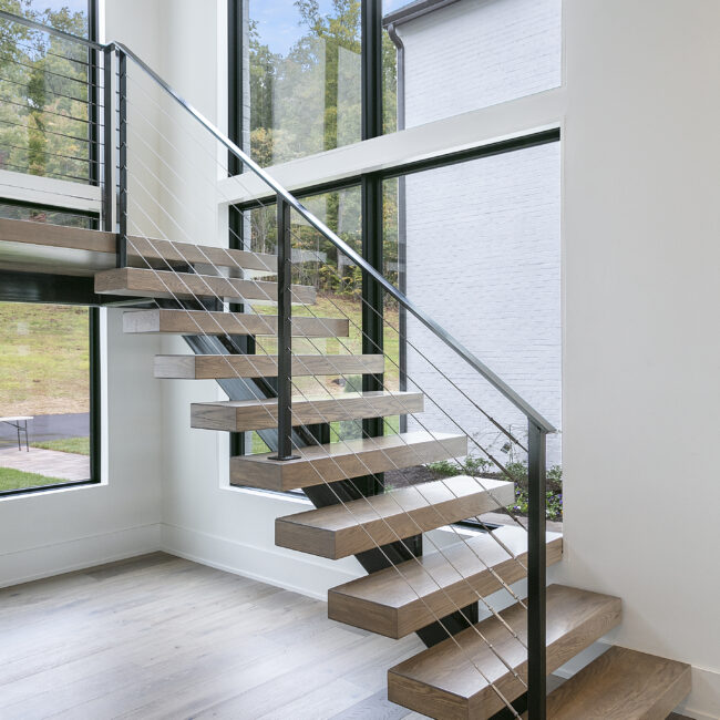 Floating wood-tread stair beside a large window in Rocky Top Hideaway, a custom home by Mike Stevens Homes