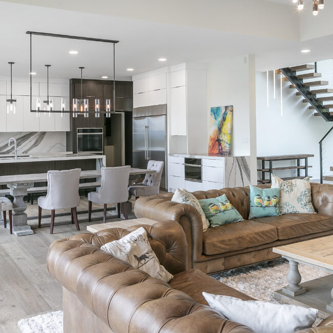 Living room with tufted leather sofas and open kitchen beyond in Rocky Top Hideaway, a custom home by Mike Stevens Homes