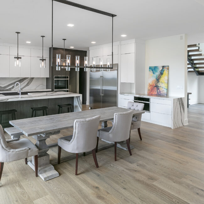 Dining table with upholstered chairs and white kitchen in Rocky Top Hideaway, a custom home by Mike Stevens Homes