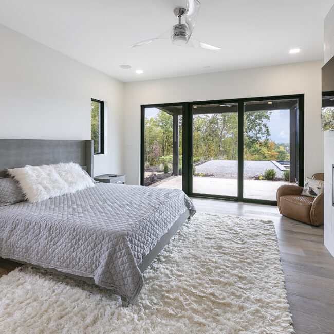 Primary bedroom with gray quilt and patio sliding doors in Rocky Top Hideaway, a custom home by Mike Stevens Homes