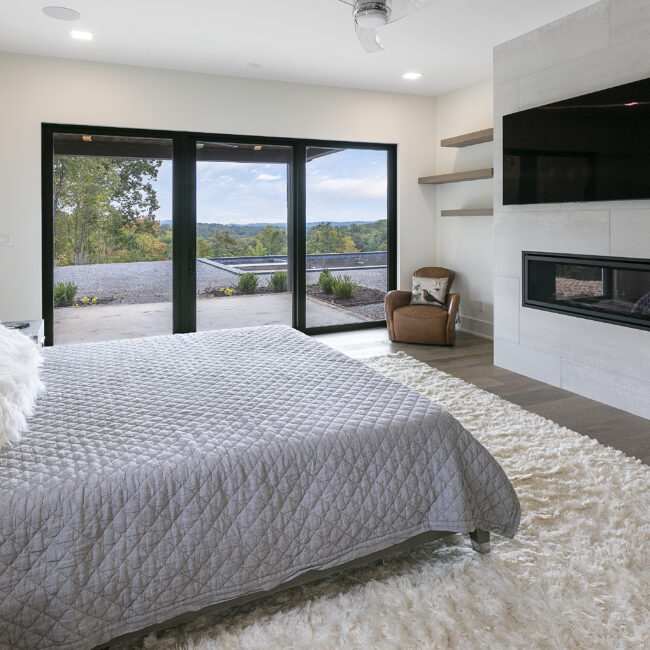 Primary bedroom with fireplace beside sliding glass doors in Rocky Top Hideaway, a custom home by Mike Stevens Homes