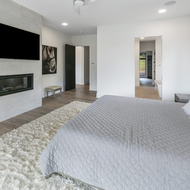 Primary bedroom with gray quilt and shag rug by fireplace in Rocky Top Hideaway, a custom home by Mike Stevens Homes