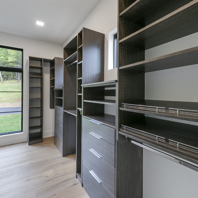 Walk-in closet with dark wood shelving and drawers in Rocky Top Hideaway, a custom home by Mike Stevens Homes