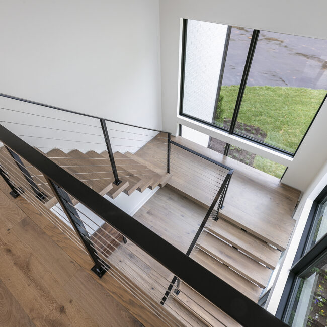 Wood-tread stairs with black cable railing by window in Rocky Top Hideaway, a custom home by Mike Stevens Homes