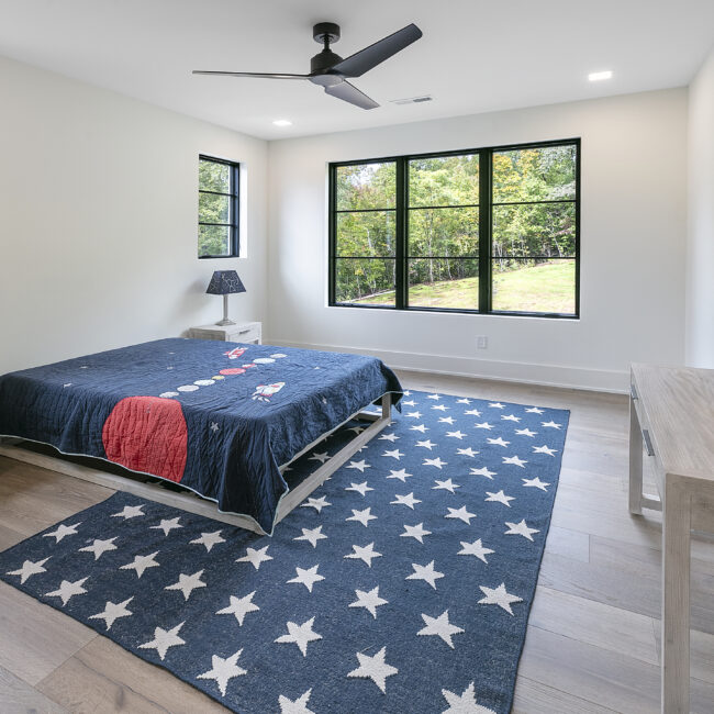 Bedroom with navy star-print rug and ceiling fan in Rocky Top Hideaway, a custom home by Mike Stevens Homes