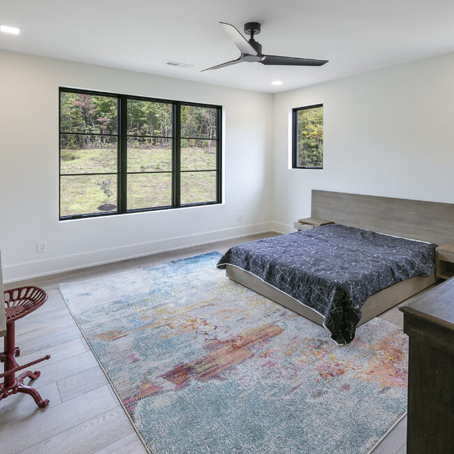 Bedroom with blue patterned rug and dark bed frame in Rocky Top Hideaway, a custom home by Mike Stevens Homes