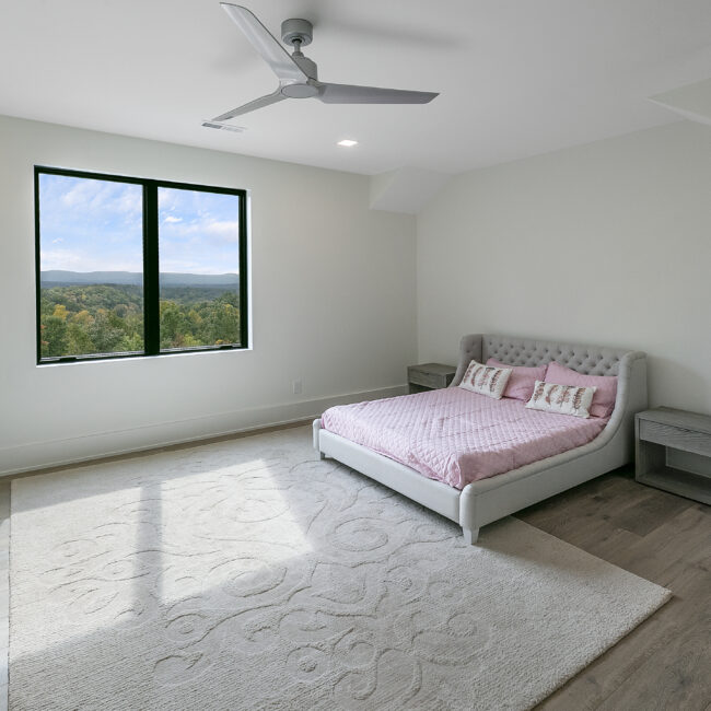 Bedroom with tufted pink bedding and window view in Rocky Top Hideaway, a custom home by Mike Stevens Homes