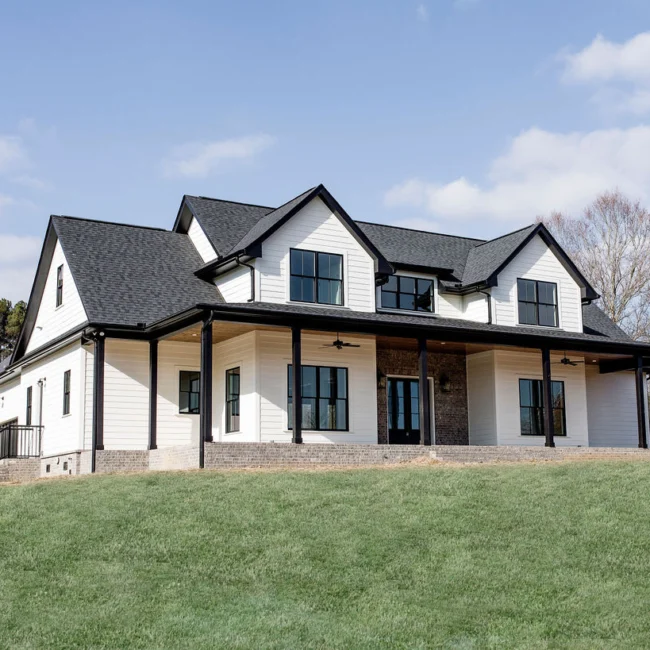 Front of white farmhouse with black trim and wide porch in Rural Farmhouse, a custom home by Mike Stevens Homes