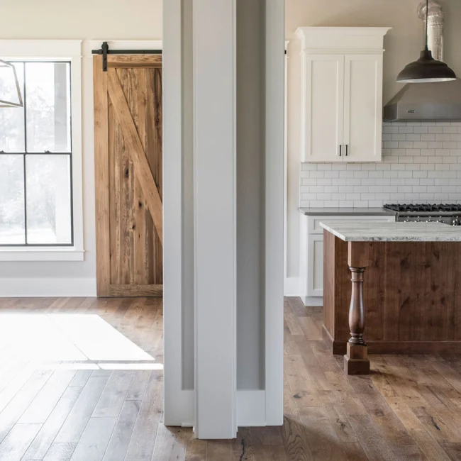 Kitchen seen through barn-style sliding door, white cabinets in Rural Farmhouse, a custom home by Mike Stevens Homes