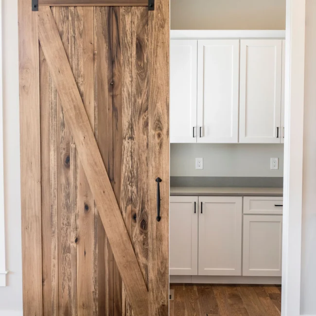 Rustic barn door opening to white pantry cabinets in Rural Farmhouse, a custom home by Mike Stevens Homes