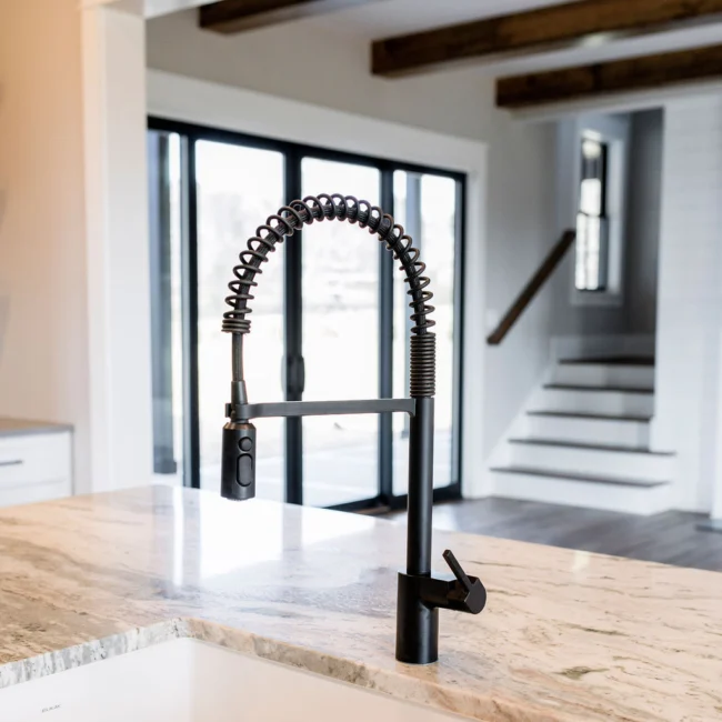 Granite island with black spring-neck faucet in Rural Farmhouse, a custom home by Mike Stevens Homes