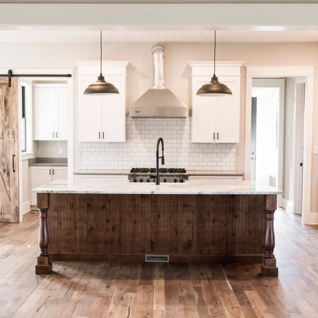 Kitchen with wood island, pendant lights and range hood in Rural Farmhouse, a custom home by Mike Stevens Homes
