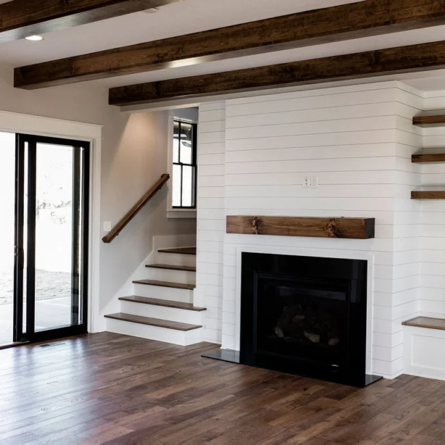 Living room with shiplap fireplace and black-railed stairs in Rural Farmhouse, a custom home by Mike Stevens Homes