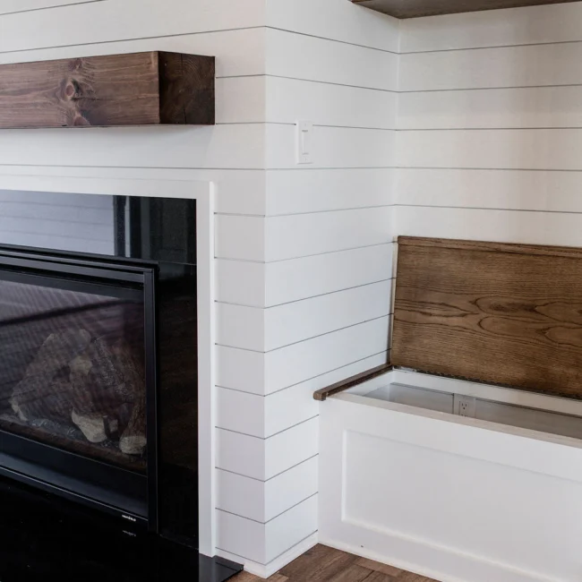 Wood bench built into shiplap wall beside fireplace in Rural Farmhouse, a custom home by Mike Stevens Homes