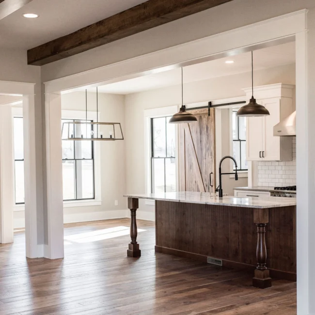 Open kitchen with barn door and pendant lights in Rural Farmhouse, a custom home by Mike Stevens Homes