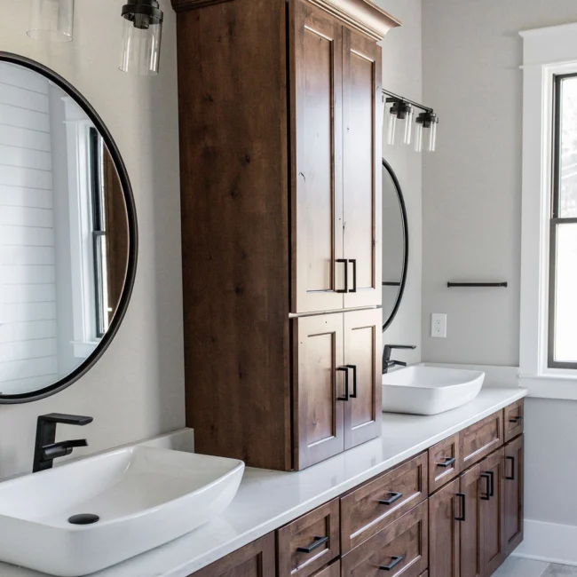 Bathroom with wood vanity, vessel sinks and round mirror in Rural Farmhouse, a custom home by Mike Stevens Homes