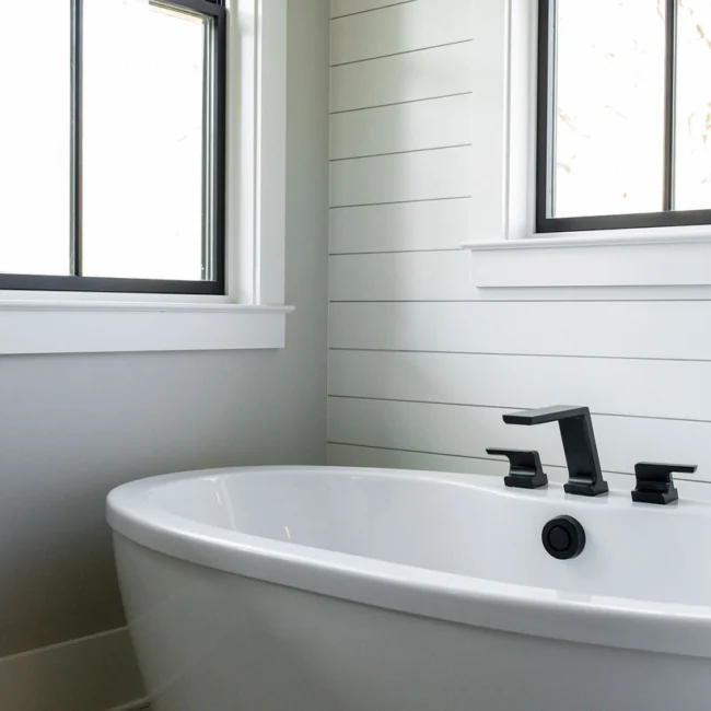 Freestanding tub with black fixtures under double windows in Rural Farmhouse, a custom home by Mike Stevens Homes