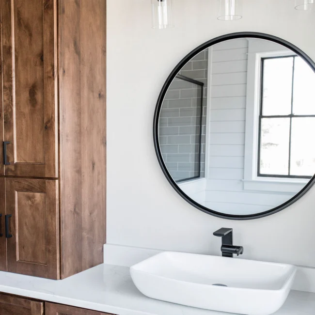 Bathroom with round black mirror and vessel sink in Rural Farmhouse, a custom home by Mike Stevens Homes