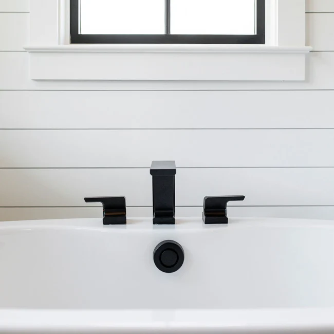 Close-up of black deck-mounted tub filler on shiplap in Rural Farmhouse, a custom home by Mike Stevens Homes