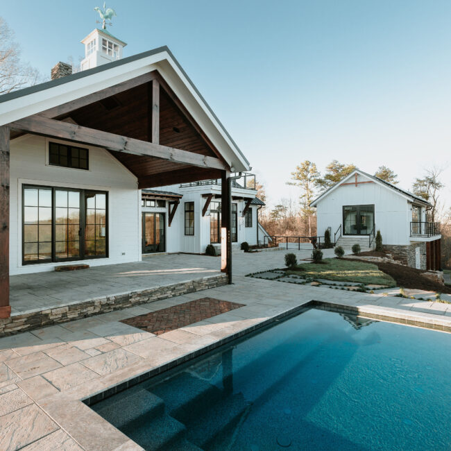 Pool with stone patio and covered porch on white home in Mountain Vista by Mike Stevens Homes