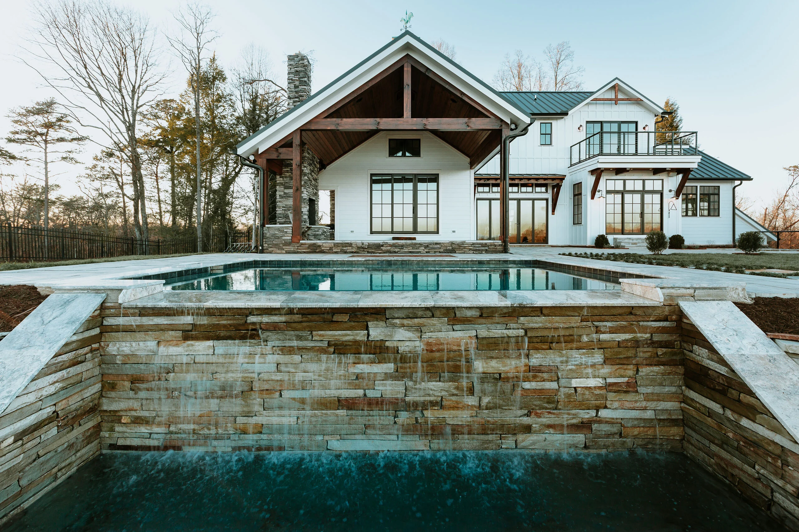 Pool with stacked stone wall and covered entry on white farmhouse in Mountain Vista by Mike Stevens Homes